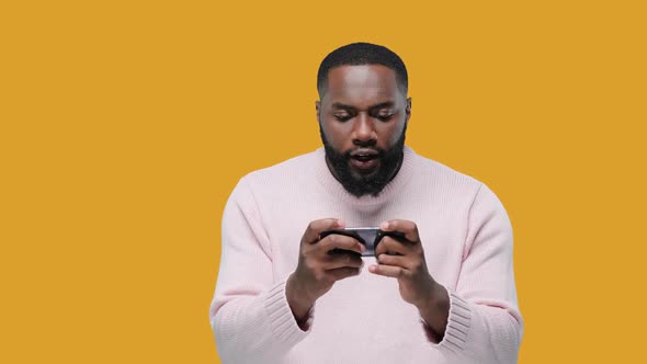Black Young Man Playing Game on Smartphone on Yellow Background
