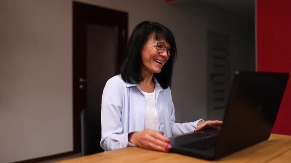 Senior woman laughing and video calling on laptop, talking with friend