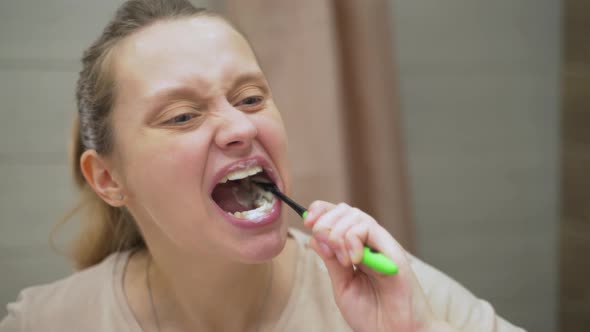 Woman in Beige Tshirt Actively Brushes Her Teeth with Green Toothbrush in the Bathroom at Home