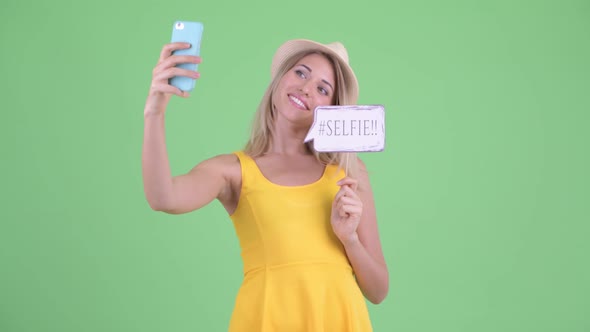 Happy Young Blonde Tourist Woman Taking Selfie with Paper Sign