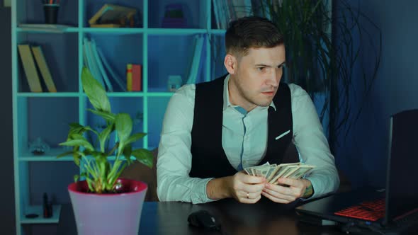 Thoughtful Man Counts Money Sitting in Armchair Before Computer in Office