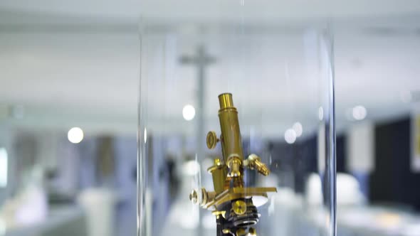 Pan down to an ancient microscope model made from brass, being displayed in an optics museum showcas