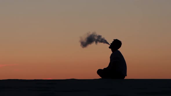 Guy Holds an Electronic Cigarette in His Hand and Smokes It. Silhouette