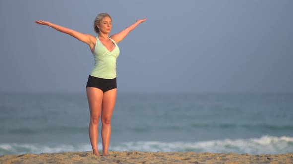 The back of a young woman doing yoga on the beach.