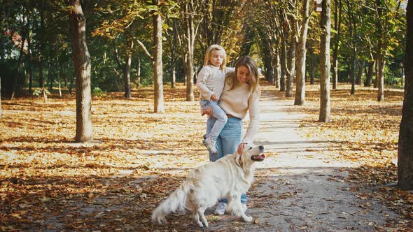 Young Mother Smiling Hugging and Holding in Arms Her Little Daughter While Walking Their Dog at