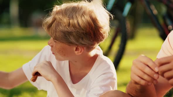 A close-up view of a positive boy is talking to his brother while having a picnic on the grass
