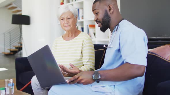 Video of african american male doctor using laptop with caucasian senior woman