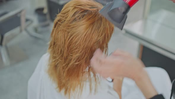 Close up of Professional stylist or hairdresser's hand using hair dryer blow young woman's wet hair.