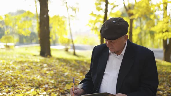 Senior Man Sitting on Bench in Park Thinking When Writing and Looking Asides