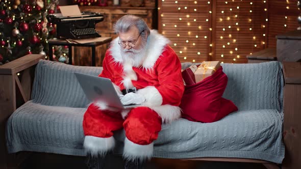 Focused Elderly Man in Santa Claus Costume Chatting Use Laptop