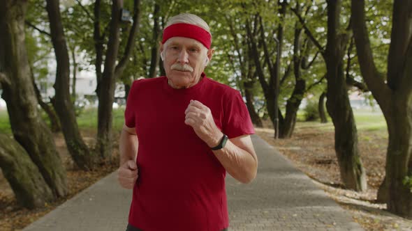 Male Senior Person Running Along the Road in Park. Mature Runner Man Training, Listening Music