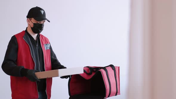 Delivery Man in Protective Equipment Is Packing Takeaway Pizza