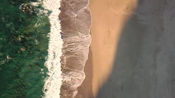 Aerial top down view of waves breaking on beach at sunset. Lockdown