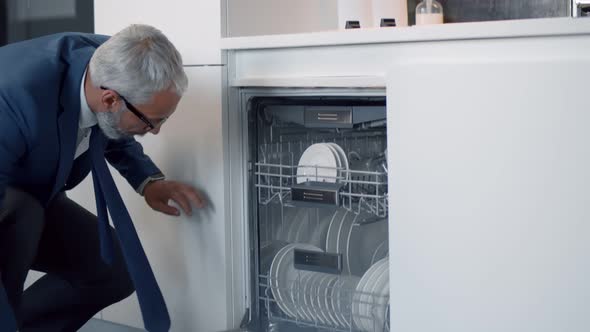 Handsome Mature Businessman Taking Clean Plate From Dishwasher in Kitchen