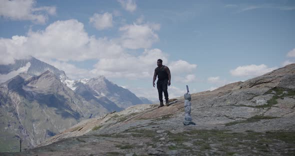 Black male traveler with back pack looking around and walking up hill near Matthorn in Switzerland