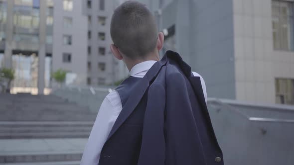 Back View of a Handsome Well-dressed Boy with Jacket on His Shoulder Standing on the Street Looking