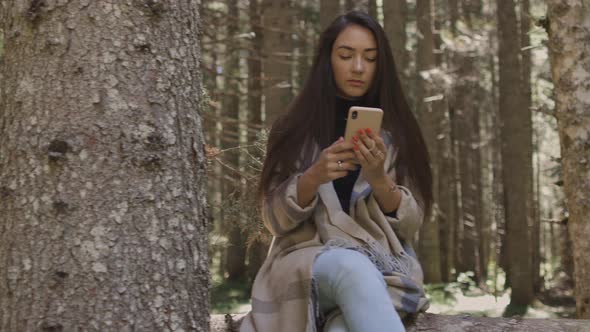 Pretty Woman Using Phone in Forest Sitting on Wooden Log