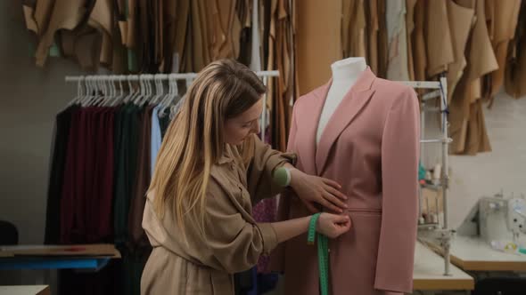 female tailor designer is outlining clothing pinned to tailoring dummy with measure-tape
