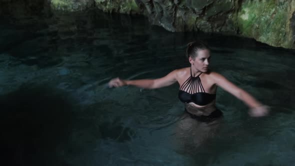 Young Woman Swims in an Underground River in Cave with Fresh Water Among Cliffs