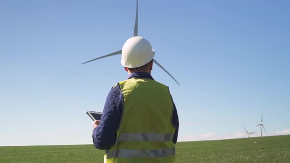 Technician Standing Near Wind Mill and Making Notes in Tablet