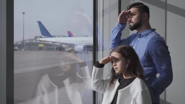 Side View Close-up of Caucasian Man and Little Girl Looking Out the Glass Airport Window at the