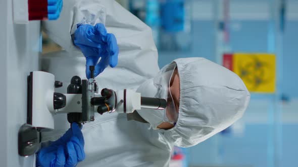 Vertical Video Scientist in Ppe Suit Making Adjustments and Looking Through Laboratory Microscope