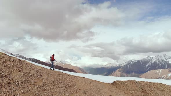 Aerial View Young Man in Sunglasses with a Backpack Goes Down the Mountain on the Crest on the