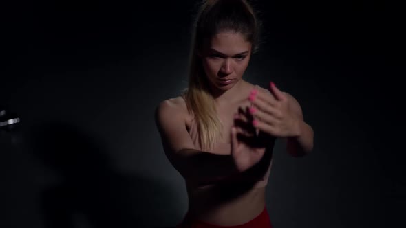 Focused Caucasian Sportswoman Warming Up Hand Muscles Sitting in Darness in Gym