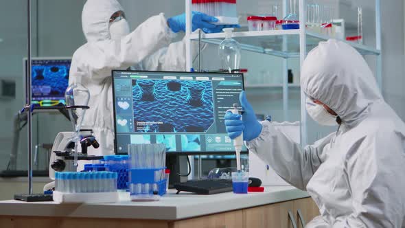 Scientist in Protection Suit Using Micropipette Filling Test Tubes