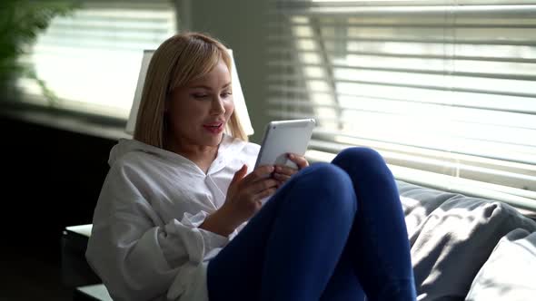 A Relaxed Young Woman Is Holding a Tablet Computer Looking at the Screen Enjoying Using Mobile Apps