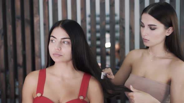 Woman Hairdresser Combs the Black Hair of a Charming Young Girl 