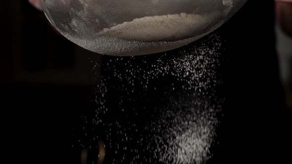 Closeup of White Flour is Falling Through a Steel Sieve on Black Background