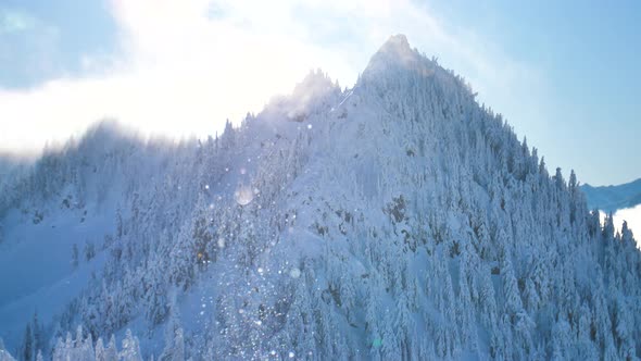 Snowflakes Falling In Front Of Sunny Mountain Top Bright Light Shining Through Clouds Above Peaks