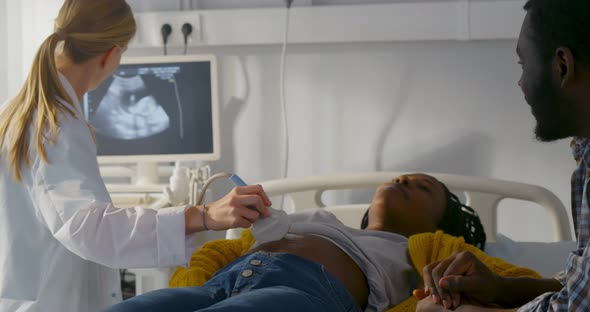 Sonographer Scanning and Examining African Pregnant Woman While Expecting Father Looking at Monitor