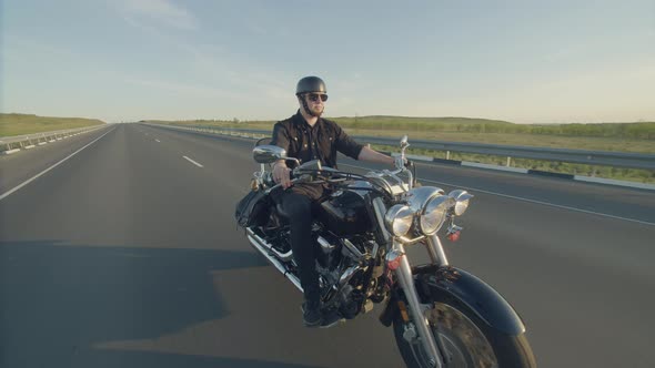 Confident Serious Biker in Black Leather Jacket Helmet and Sunproof Glasses Rides Along Highway on