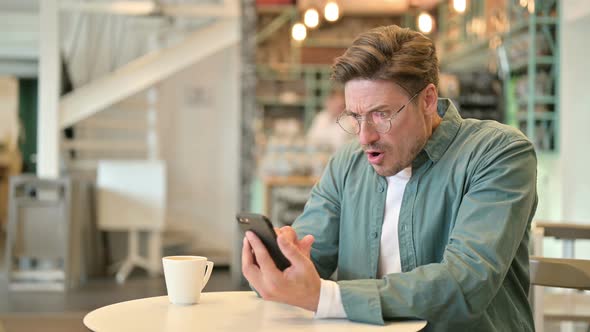 Upset Middle Aged Man Having Loss on Smartphone in Cafe 