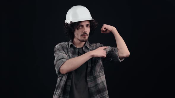 The Hipster Boy with a White Engineer's Helmet Strong and Confident Tenses His Biceps and Looks at