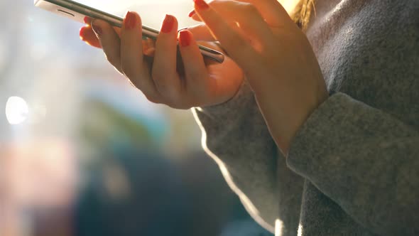 Female Hands Using Smartphone Against a Blurred Cityscape in the Setting Sun