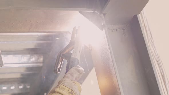 Sparks fly as welder wearing safety gloves weld steel structure; slowmo