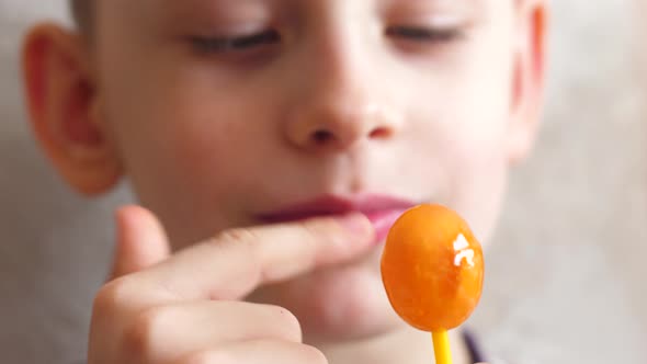 Portrait of a cheerful caucasian boy 7 years old licking a caramel candy on a stick. Selective focus