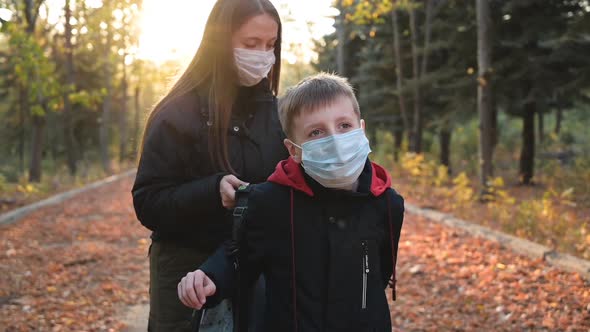 Young Woman Helping Her Son Putting on Backpack on the Street