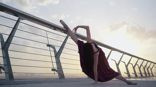 Professional Ballerina Standing in Split on Bridge with Sun Shining at the Background, Wide Shot