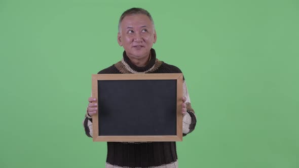 Happy Mature Japanese Man Thinking While Holding Blackboard