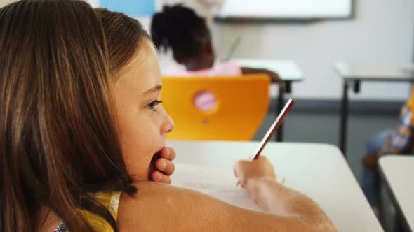 Schoolgirl whispering into her friends ear in classroom