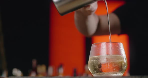 Barman Pours Mixed Cocktail From the Shaker to the Ice Cube on the Cocktail Glass in Slow Motion