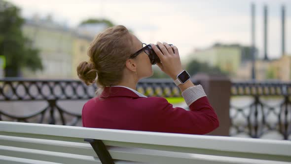 Back View of Young Businesswoman Sitting on Bench Drinking Takeaway Coffee Outdoors