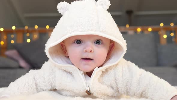 Cute Baby Girl In Beige Cosy Clothing Lying On Knit Blanket