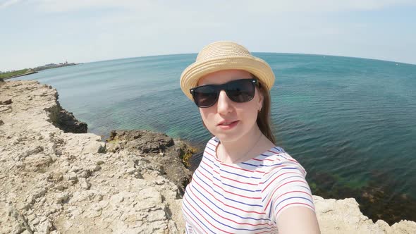 A Woman in a Hat and Sunglasses is Filming Herself on the Seashore