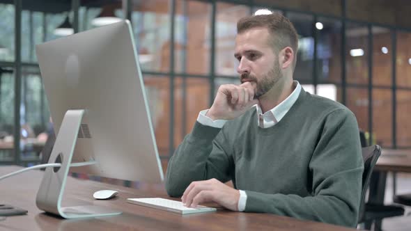 Young Man Thinking While Working on Computer