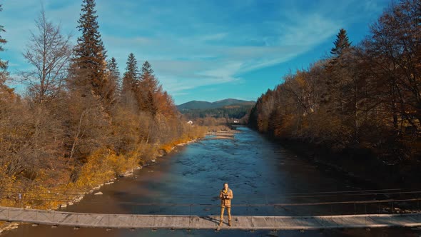 Drone Selfie Footage By Happy Man Hiker Sitting on Wooden Suspension Bridge Over Mountain River
